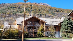 Un chalet en bois doté d’un balcon, entouré d’arbres et avec une montagne en toile de fond.
