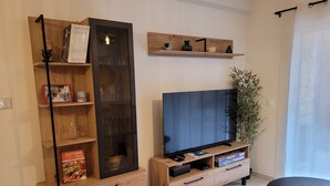 Un salon moderne avec un meuble TV en bois, un meuble vitré et une étagère ornée d’objets décoratifs.