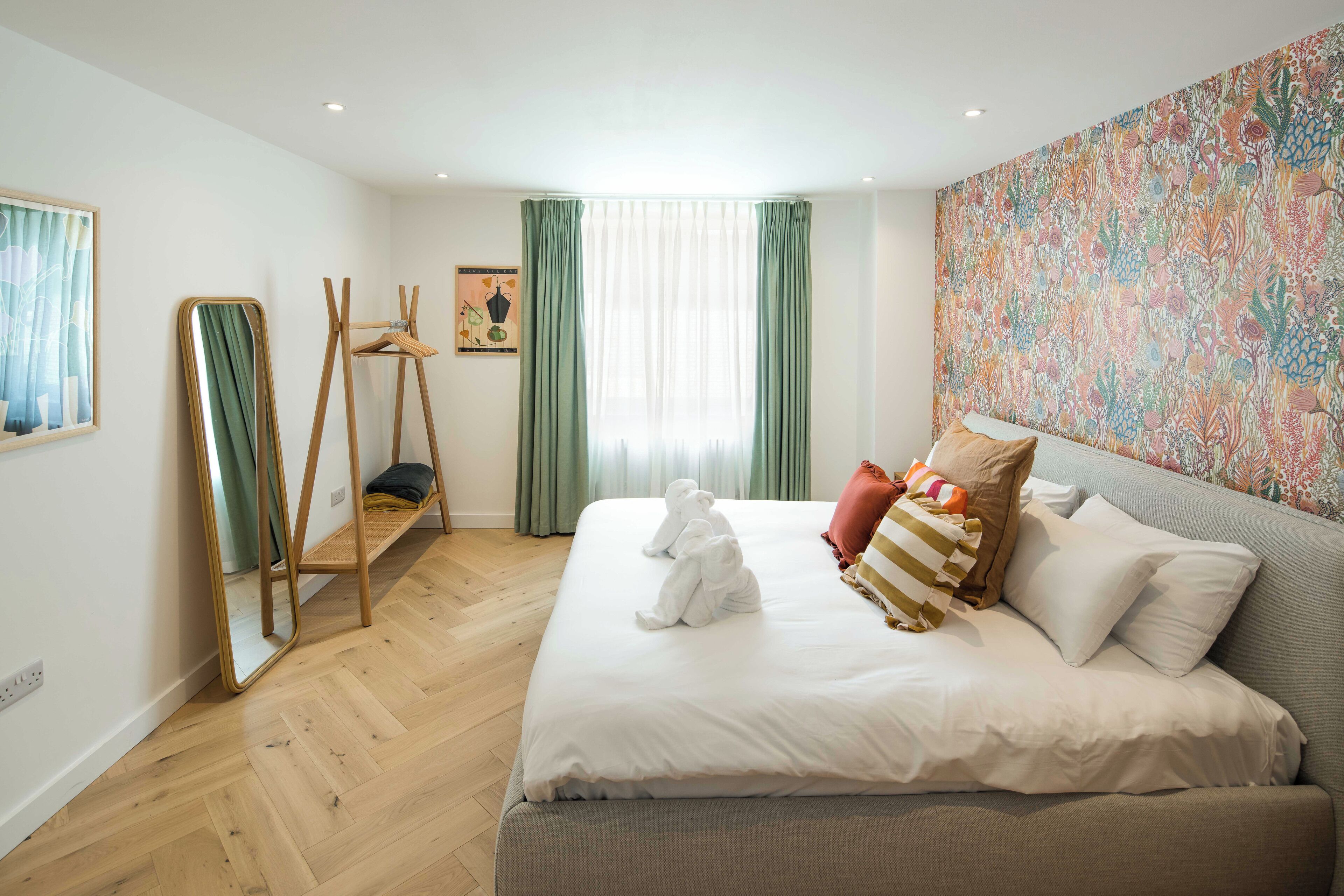 Een slaapkamer met een groot bed, een spiegel, een houten stoel en een kleurrijke wandtapijt.
