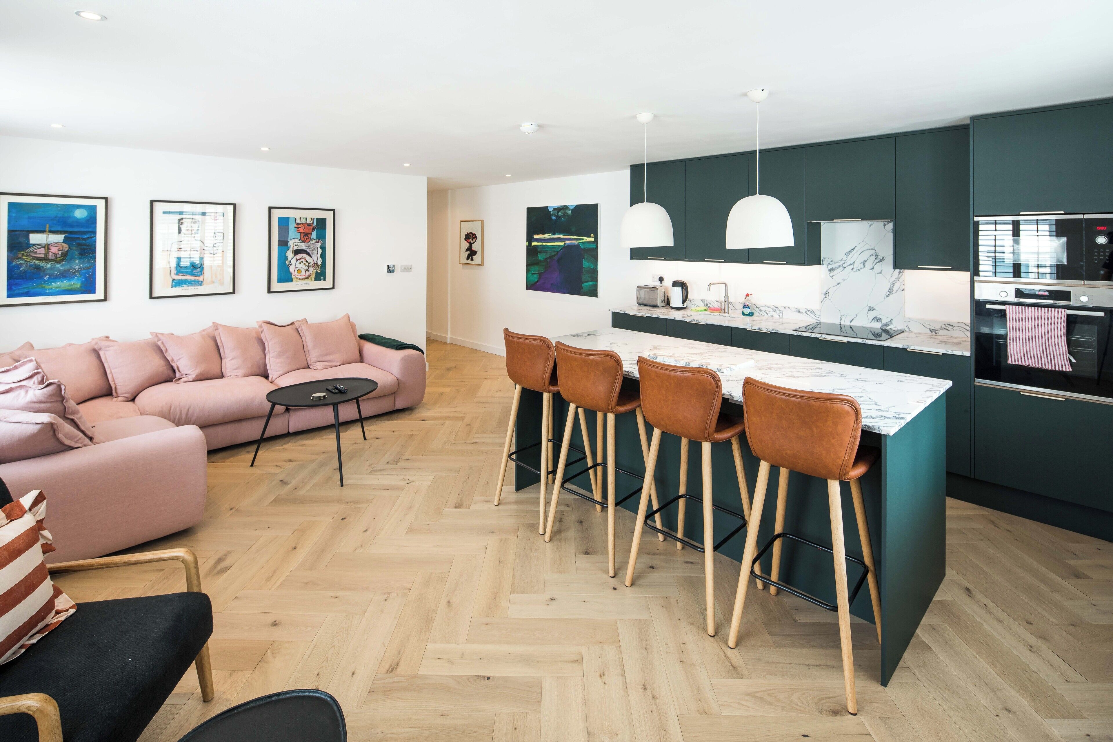 En moderne stue med sofa, sofabord og et køkkenområde med barstol og køleskab.