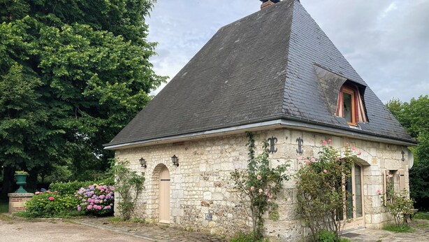 Een gebouw van steen met een steil puntig dak, een kleine gewelfde ingang en een raam met luiken.