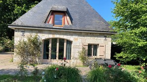 Een stenen huis met een schuin dak, een klein dakraam en een grote, ronde deuropening.