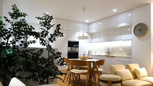 A modern kitchen with white cabinets, a built-in oven, and a dining area with wooden chairs and a table. - CA.Tanoeiros 2 (Funchal)