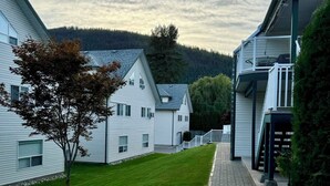 A residential area with a paved pathway leading to a gated entrance, surrounded by white houses with green lawns and a hilly backdrop. - Sicamous Townhouse & Boat Slip. Welcome to the lake! (Sicamous)