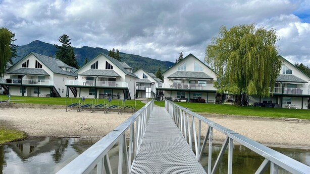 A row of white cabins with balconies, a wooden deck, and a river in the foreground. - Sicamous Townhouse & Boat Slip. Welcome to the lake! (Sicamous)