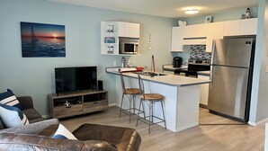 A compact living space with a kitchenette, a flat-screen TV, a leather sofa, and a dining area with stools. - Sicamous Townhouse & Boat Slip. Welcome to the lake! (Sicamous)