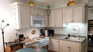 A kitchen with white cabinets, a stove, a microwave, and a sink.