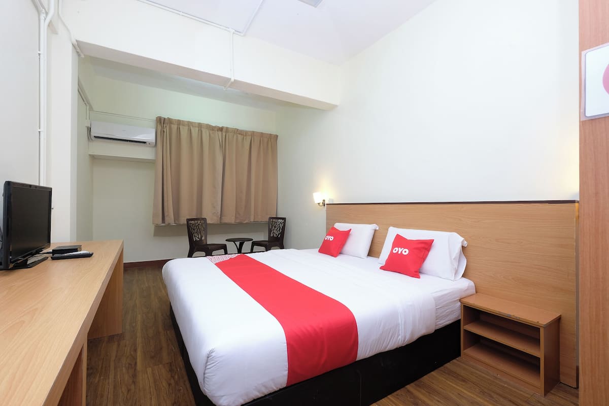 A hotel room with a bed, bedside table, TV, and a desk.
