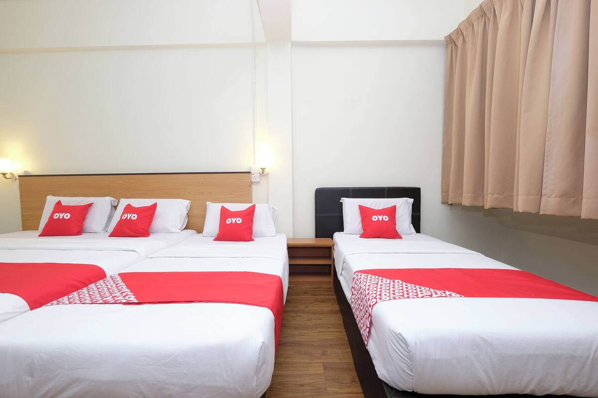 A hotel room with four beds arranged in a row, each with white bedding and red accents.