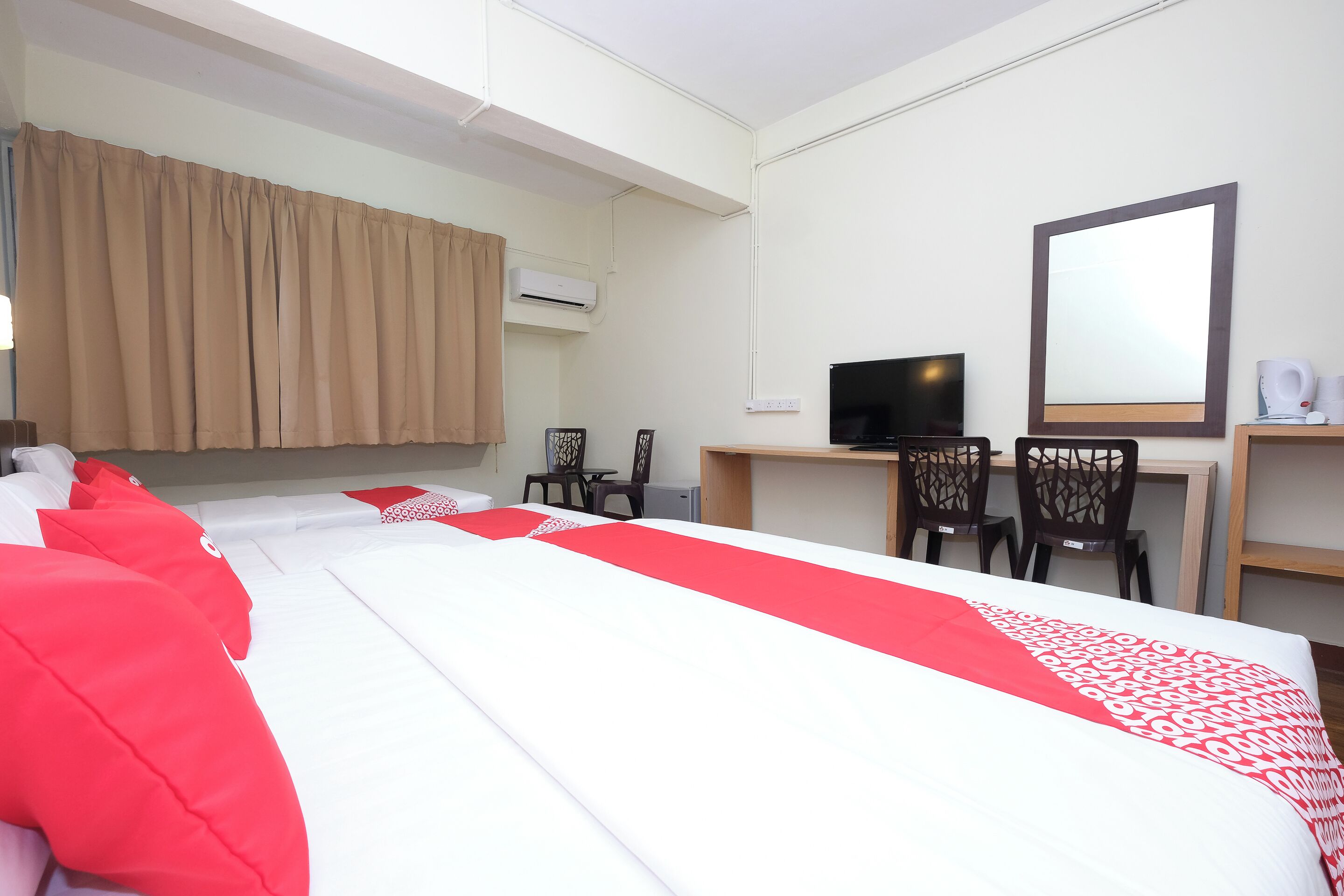 A hotel room with a large bed, a desk with two chairs, a television, and a mirror.