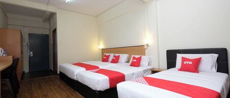 Quarto de hotel com duas camas, cada uma com roupa de cama vermelha e branca, uma escrivaninha de madeira e uma porta ao fundo.