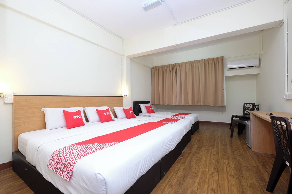 A hotel room with a large bed, a desk, and an air conditioning unit.
