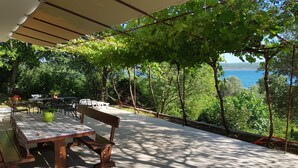 Ein Außenbereich mit Tischen und Stühlen, eine Pergola, die Schatten spendet, und Blick aufs Meer.