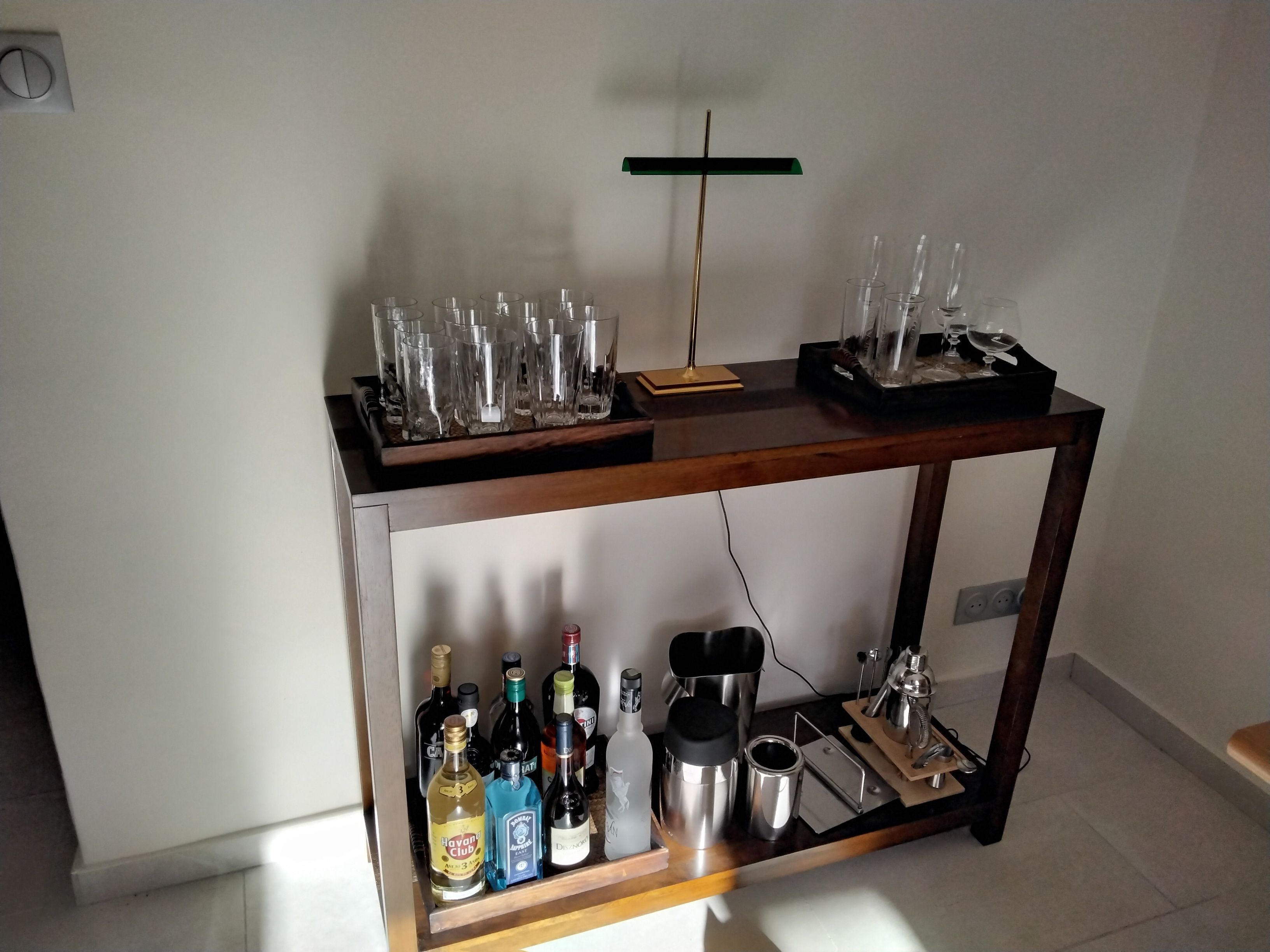 Un chariot de service en bois contenant de nombreux verres et bouteilles.