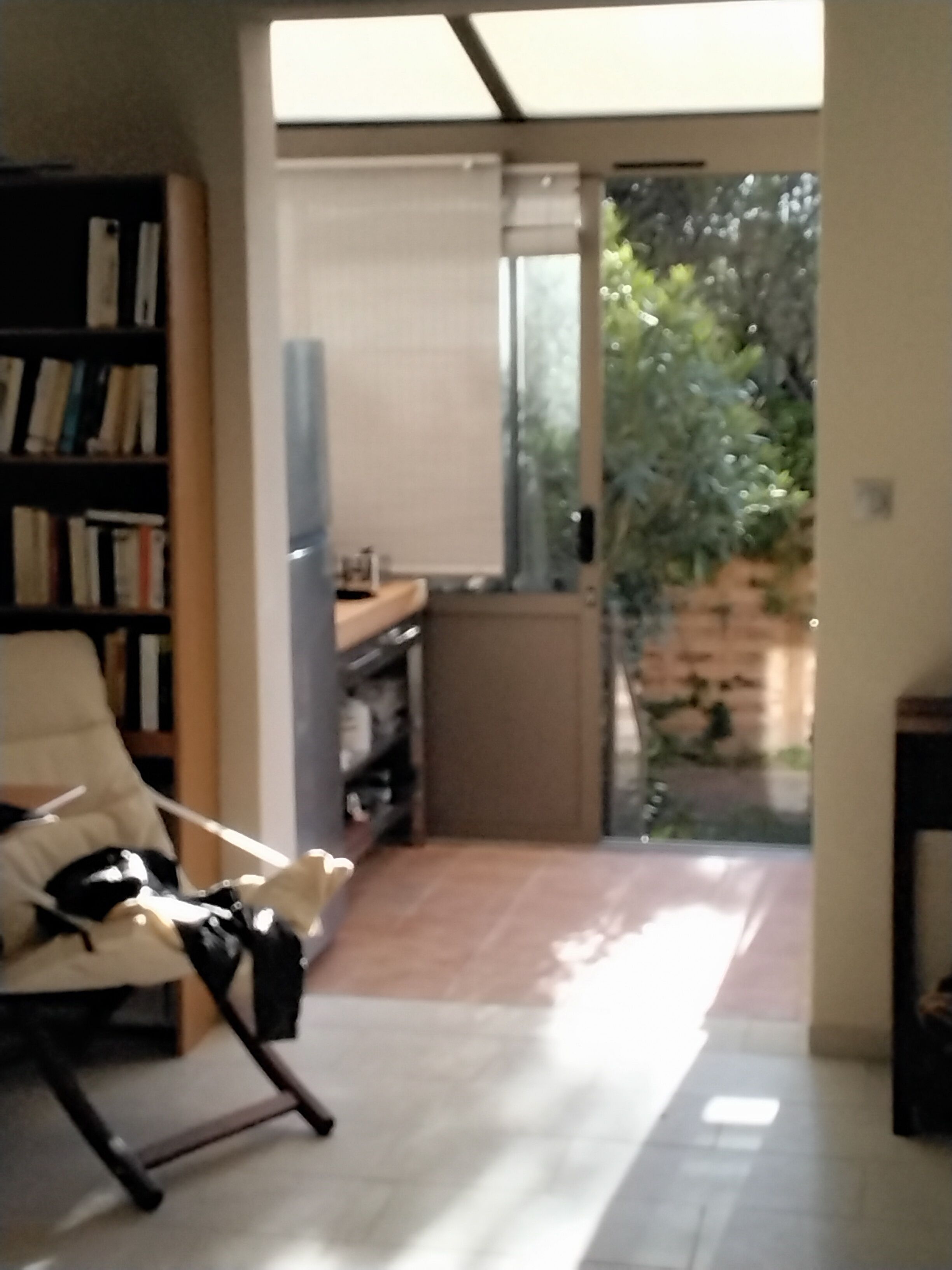 Ein Wohnzimmer mit Bücherregal, einem Sessel und Blick auf einen Garten durch eine Glastür.