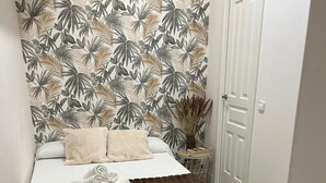 Une chambre à coucher avec un lit, un tapis moelleux, un papier peint orné de motifs de feuilles tropicales et une porte blanche.