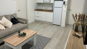 Un espace de vie compact comprenant un coin cuisine, un canapé gris, une table basse et un tapis à motifs.