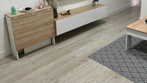Un salon moderne avec un téléviseur à écran plat fixé à un mur blanc, un buffet en bois, un tapis à motifs et une petite plante en pot.