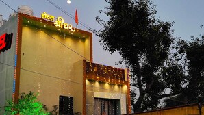 A hotel with a sign in a local language, a large tree in front, and a view of a river. - Hotel Shridhar (Ujjain)