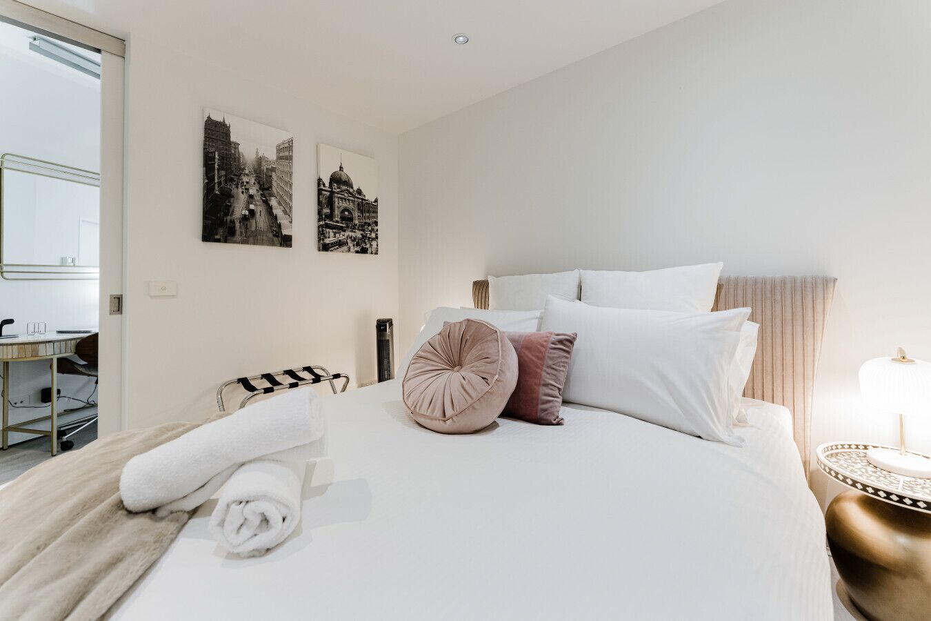 Habitación de hotel con una cama grande, una mesita de noche con lámpara y dos cuadros en la pared.
