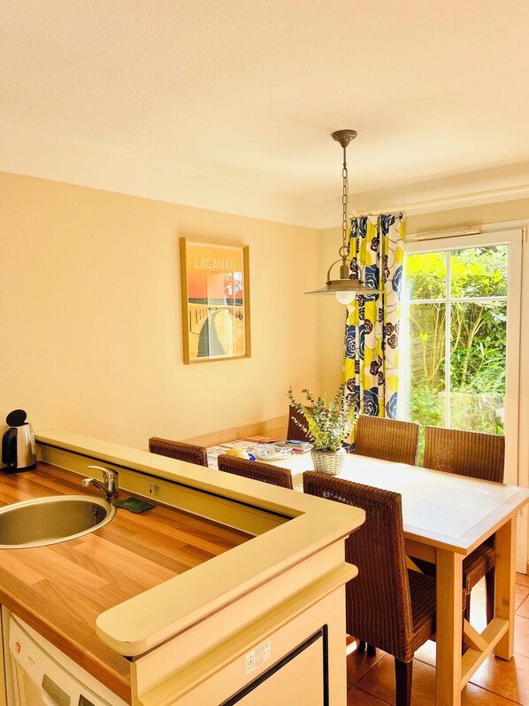 Una cocina con encimera de madera, un fregadero, una mesa de comedor con sillas y una ventana con cortinas.