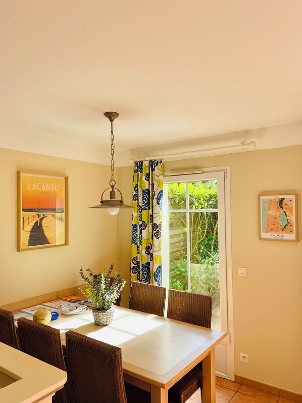 A dining area with a table, chairs, a hanging light fixture, and a window with curtains.