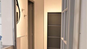 A hallway with a tiled floor, a door with a mirror, and a wall-mounted cabinet.