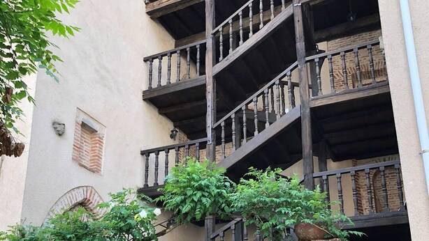 A multi-story building with a metal gate, brick walls, and a staircase with wooden railings.
