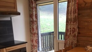Una cocina con encimera negra, armarios de madera y un horno. Se ve una ventana con cortinas estampadas y una balcón.