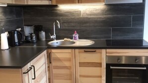 Una cocina moderna con armarios de madera, encimera negra, horno de acero inoxidable y un lavamanos.
