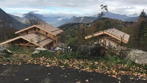 Una cabaña de madera con techo inclinado, rodeada de un paisaje montañoso y follaje otoñal.