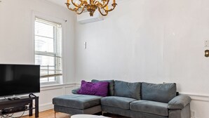 A living room with a grey sectional sofa, a flat-screen TV on a stand, a white coffee table, and a chandelier. - Spacious 5-bedroom house in enjoyable Brooklyn (Brooklyn)