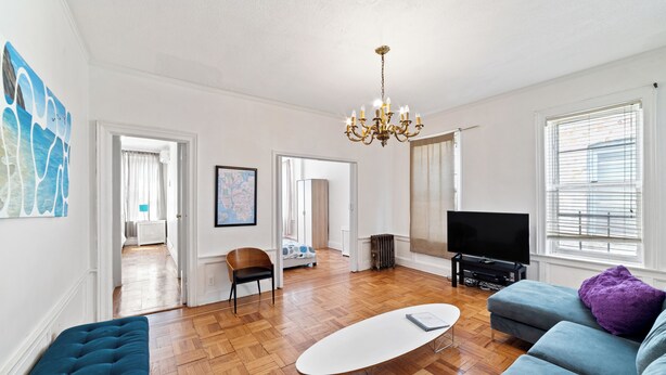 A spacious living room with a wooden floor, a white coffee table, a blue sofa, a blue bench, and a television. - Spacious 5-bedroom house in enjoyable Brooklyn (Brooklyn)