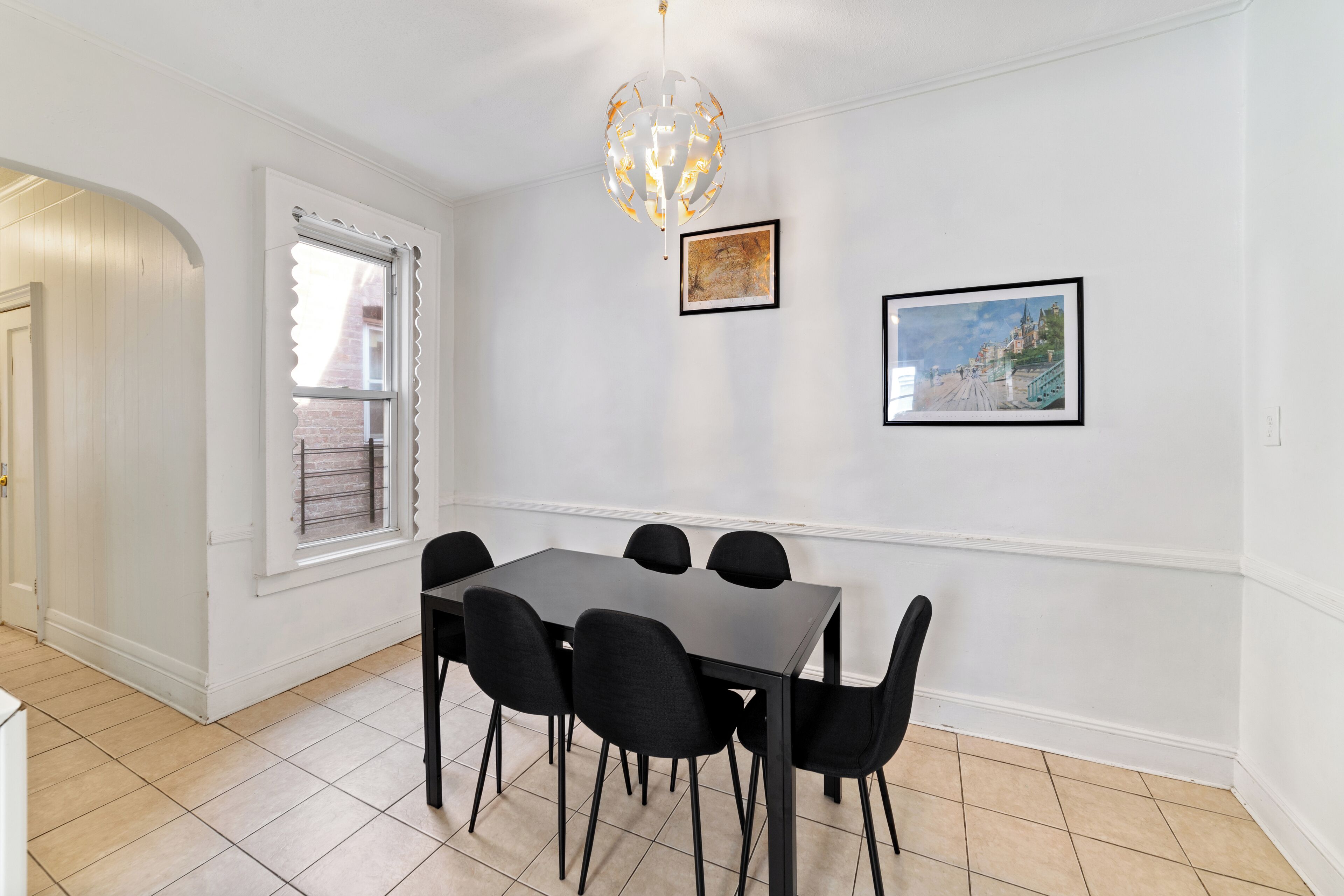 Un coin repas comprenant une table rectangulaire et six chaises, un lustre et deux tableaux encadrés accrochés au mur.