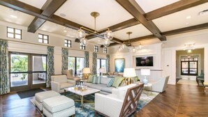 A spacious living room with a high ceiling, large windows, and a modern chandelier. - HOGARTS & AVATAR! MARIO Kart! Pool with Waterpark Close to Disney! (Kissimmee)