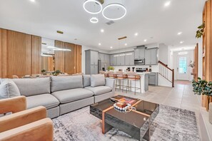 Una sala de estar moderna con un sofá gris, una mesa de centro y una cocina con gabinetes grises y una barra.