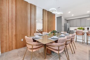 Un comedor moderno con un separador de madera, una mesa con cubierta de vidrio y sillas tapizadas en rosa.