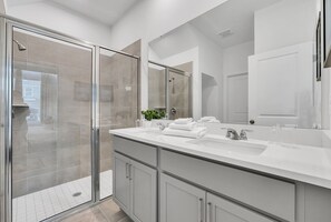 A modern bathroom with a glass shower enclosure, a large mirror, and a double sink vanity.
