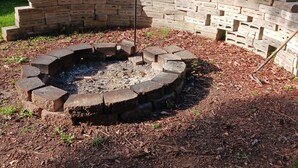 Un patio trasero con un pozo de fuego circular de ladrillo rodeado por un muro de ladrillo.