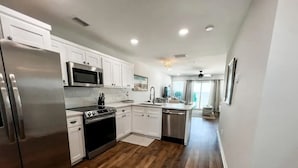 A modern kitchen with white cabinets, stainless steel appliances, and a wooden floor.