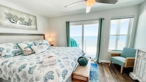 A bedroom with a bed, a bench, a chair, a ceiling fan, and a view of the ocean.