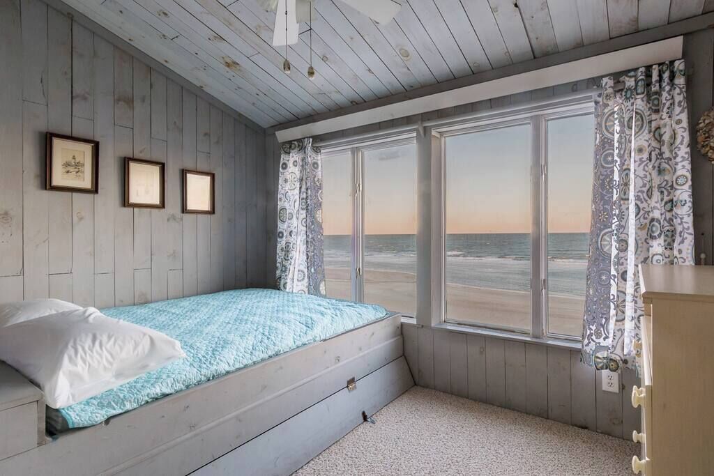 Une chambre avec un lit simple, une fenêtre avec des rideaux et un mur orné de tableaux.