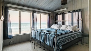 Een slaapkamer met een bed, grote ramen en uitzicht op de oceaan.