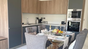 Eine moderne Küche mit Essbereich, ausgestattet mit Backofen, Kaffeemaschine und einem für vier Personen gedecktem Esstisch.