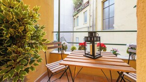 Een balkon met een houten tafel en stoelen, plantenbakken en een lantaarn.