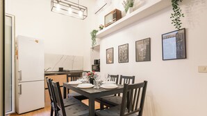 Een kleine keuken met een eettafel voor vier personen, houten stoelen en een witte koelkast.