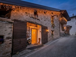 A rustic stone building with a wooden door, a bicycle parked outside, and string lights. - STABLES SUITE with one freestanding bath
typical Trentino charming style (Montagnaga di Pinè)