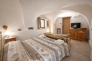 A bedroom with a bed, a wooden cabinet, a television, and a window with curtains. - STABLES SUITE with one freestanding bath
typical Trentino charming style (Montagnaga di Pinè)