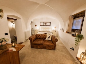 A cozy bedroom with a bed, a leather sofa, a bedside table, and a wall-mounted TV. - STABLES SUITE with one freestanding bath
typical Trentino charming style (Montagnaga di Pinè)
