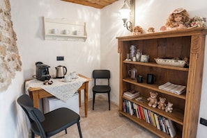 A cozy room with a wooden table, chairs, a coffee machine, a bookshelf, and a small shelf with decorative items.